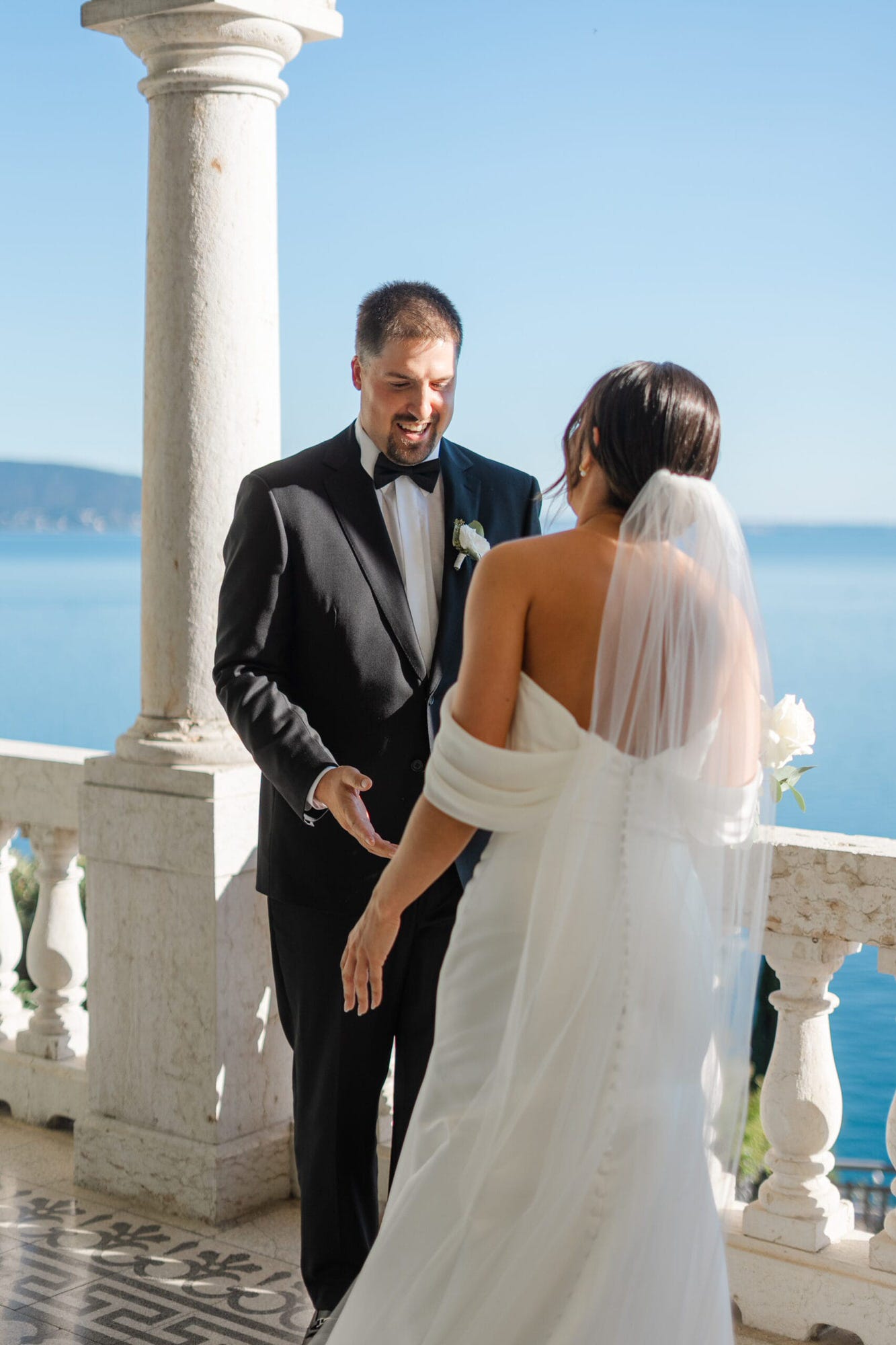 La terrazza incorniciata dagli archi e il panorama mozzafiato sul lago creano una scena perfetta mentre lo sposo, di spalle, si prepara a vivere il momento più emozionante: il primo incontro con la sua sposa, che gli cambierà la vita.