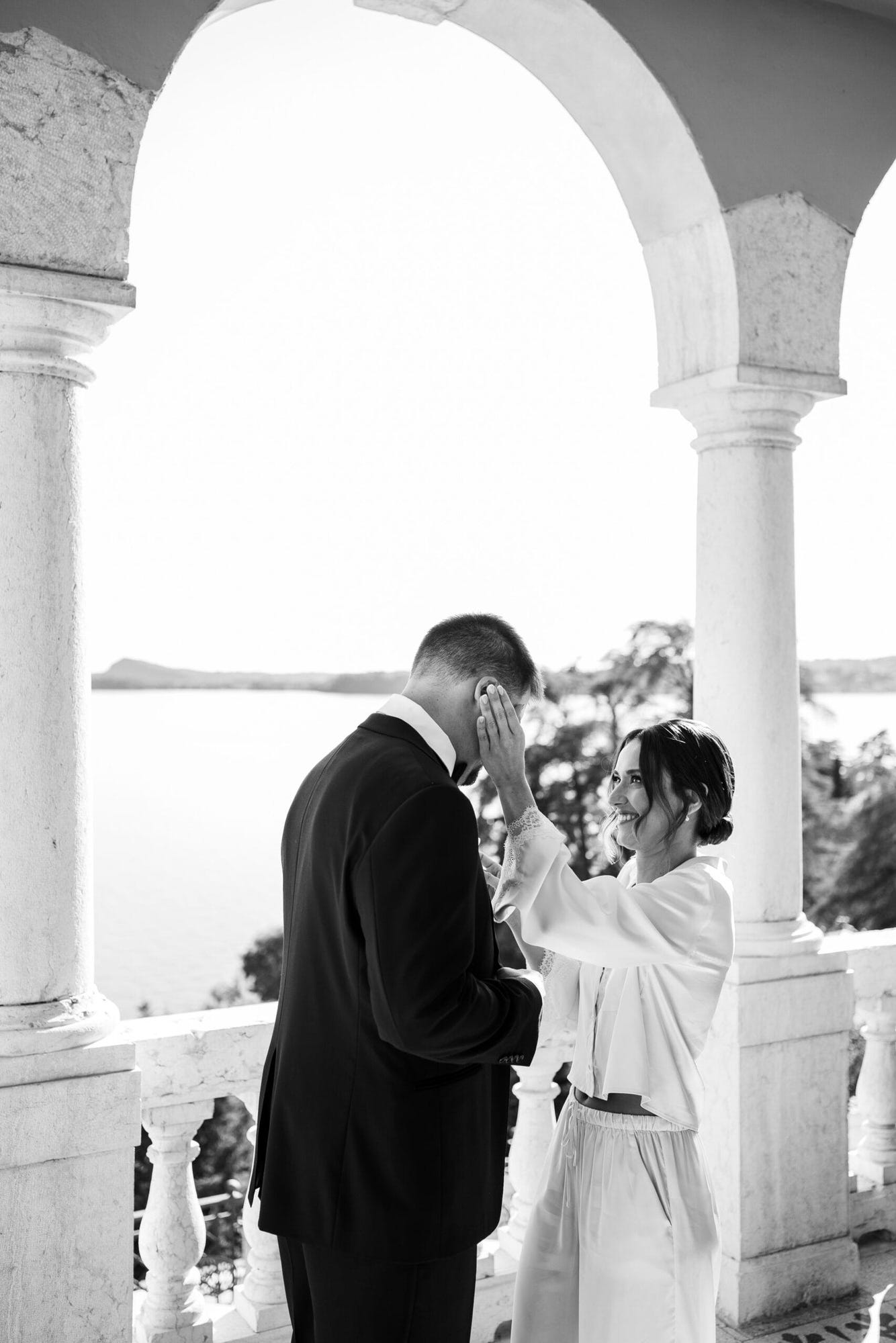 Un gesto delicato e pieno d'amore. La sposa aiuta lo sposo a mettersi il papillon, mentre la vista sul Lago di Garda fa da cornice a questo momento intimo e romantico, sottolineando la complicità e la dolcezza di questa coppia